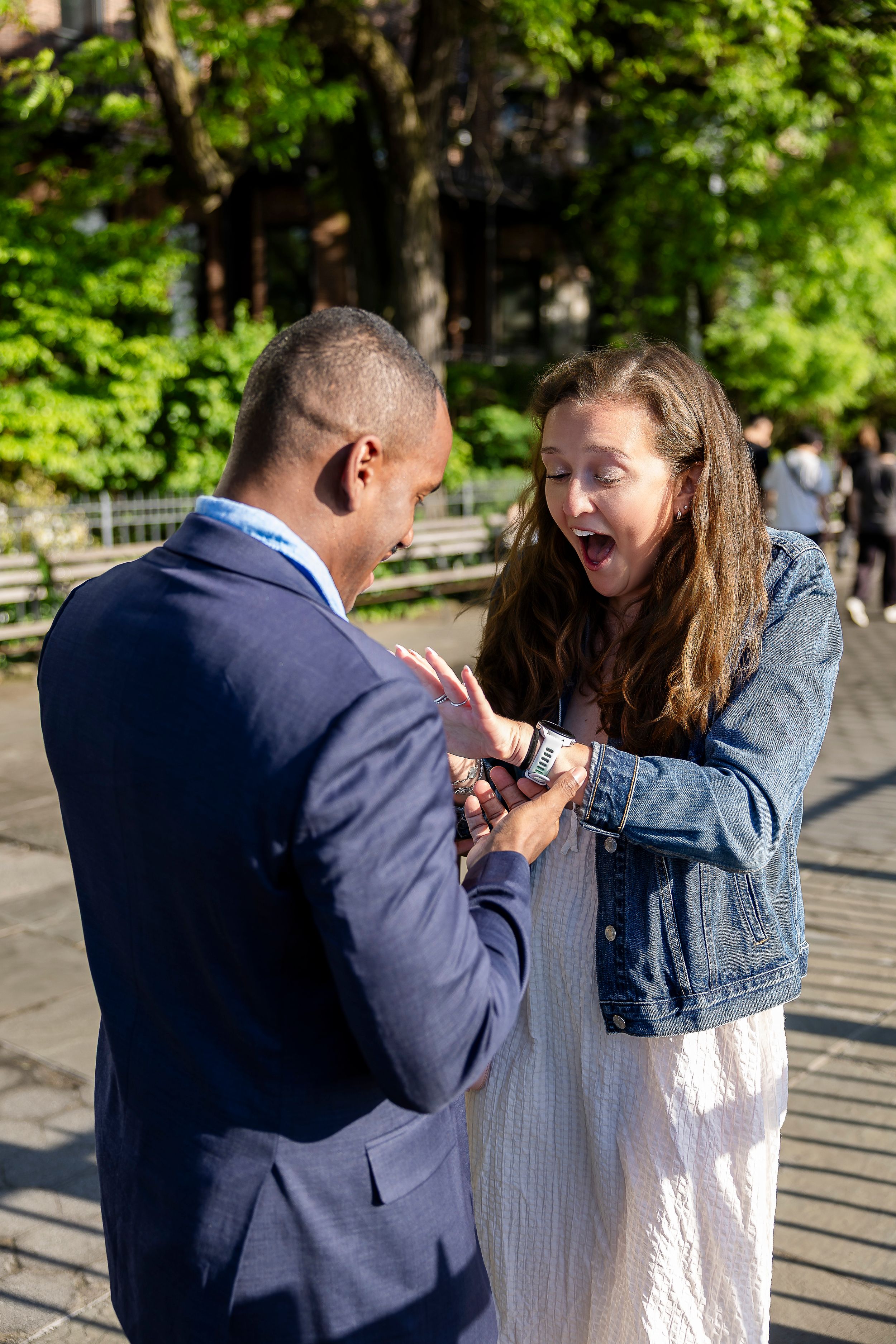 Couple sharing a joyful surprise moment outdoors, woman reacting with excitement in a sunny park setting.