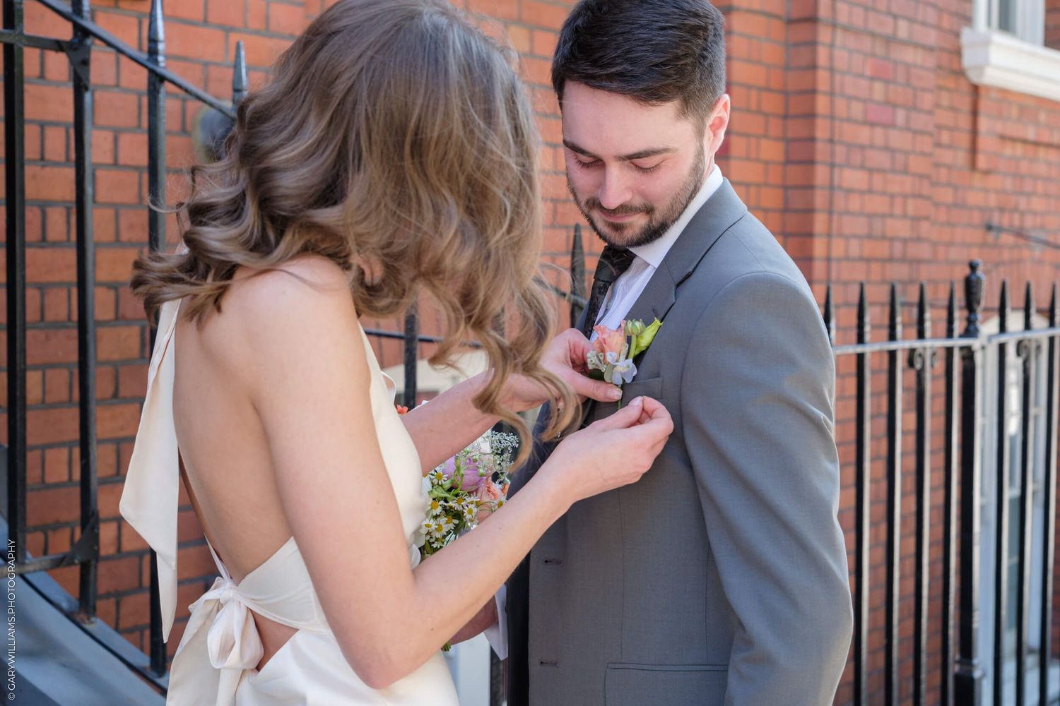 A romantic wedding photo in front of a brick building shows a tender moment between newlyweds.