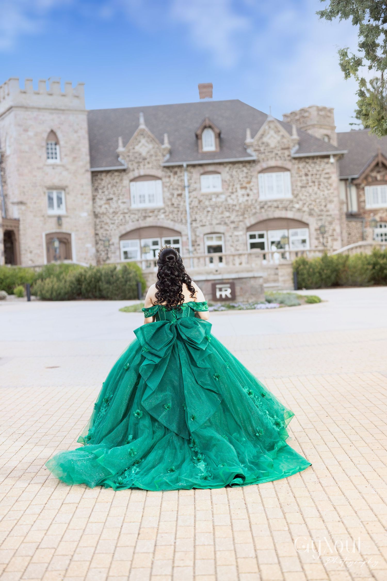 A green ballgown dress in multiple photo views outside a stone castle-like building facade.