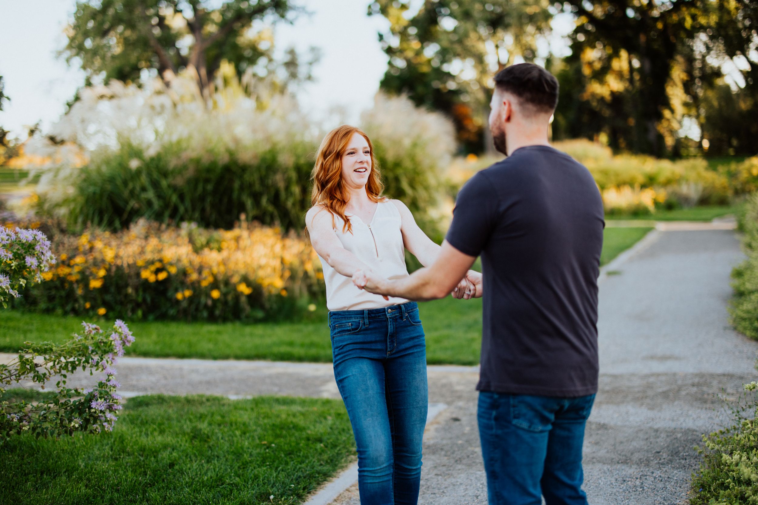 A couple shares a tender moment while standing on a garden path during golden hour among blooming flowers.