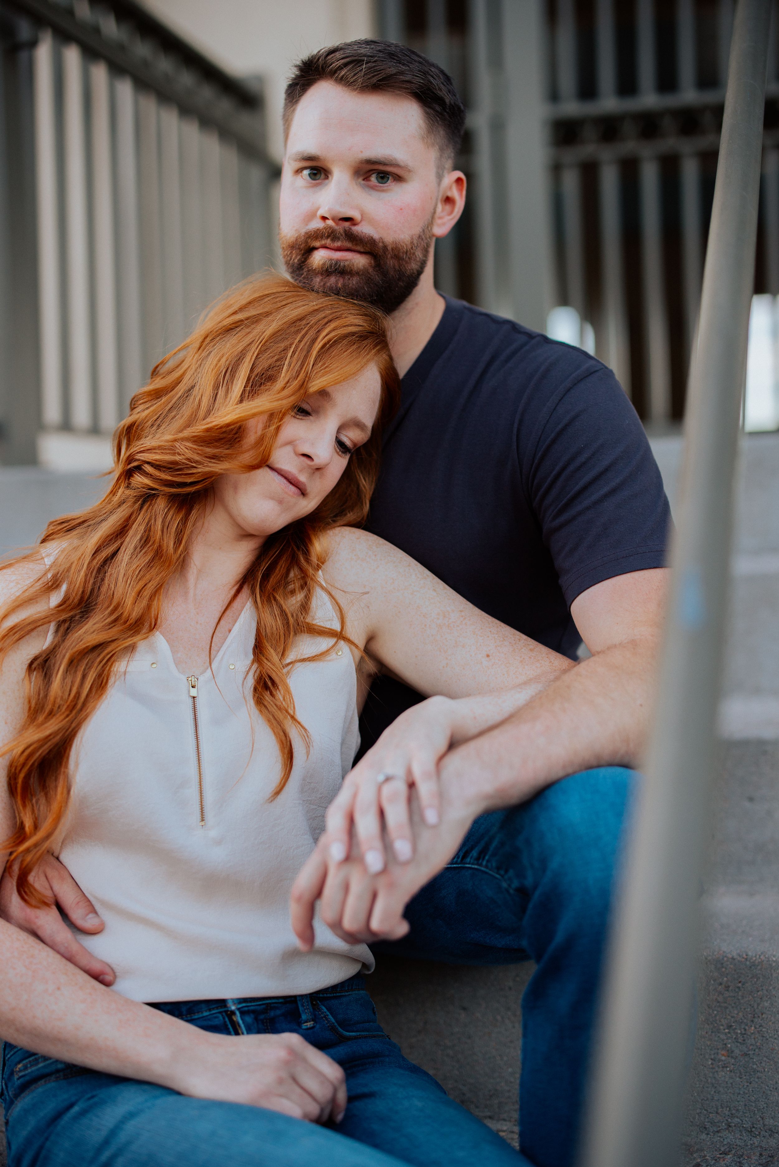 An intimate portrait of a couple in casual attire sharing a tender moment against an architectural backdrop.