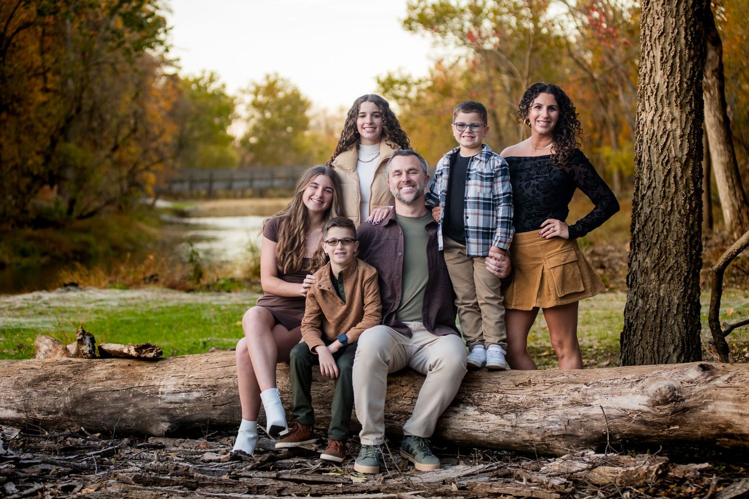 Autumn family photography session by a lake with fallen leaves and natural scenery.