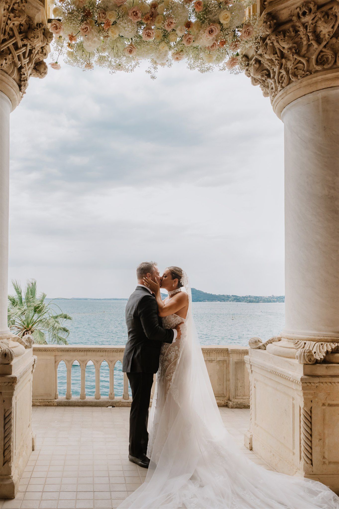 Romantic wedding moment under floral-adorned columns overlooking the ocean.