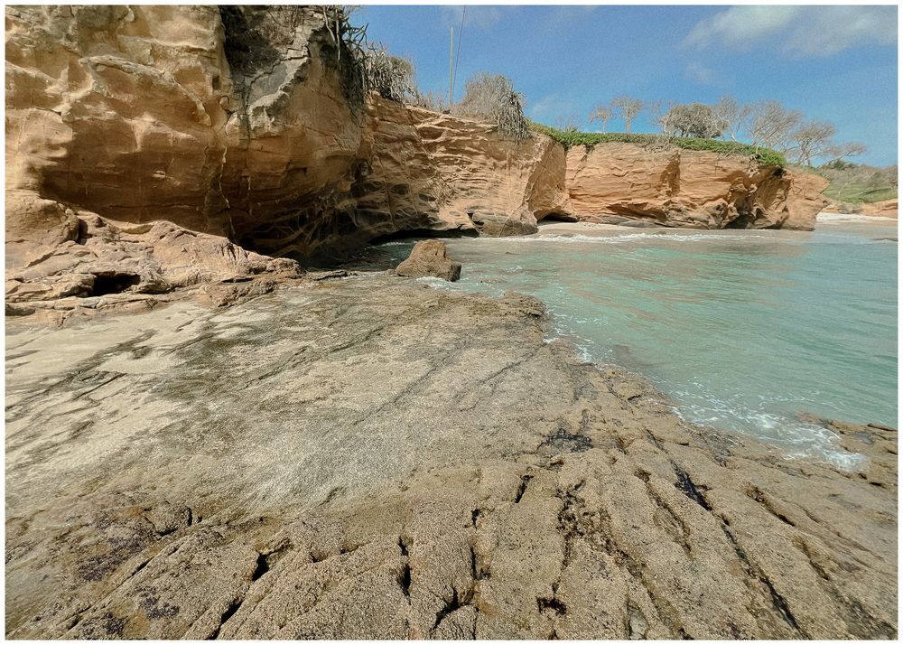Rocky coastal shoreline with turquoise waters and layered sedimentary rock formations stretching along the beach.