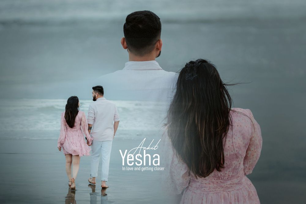 A couple in matching white and pink outfits stand at the beach with their reflection visible in wet sand at sunset.