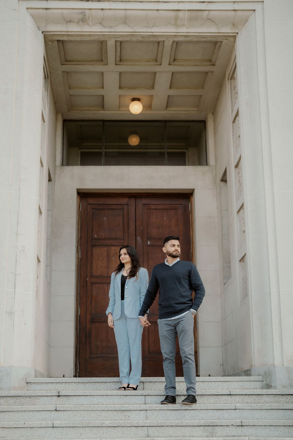 Couple standing on stone steps in front of large wooden door in classic architectural entryway.