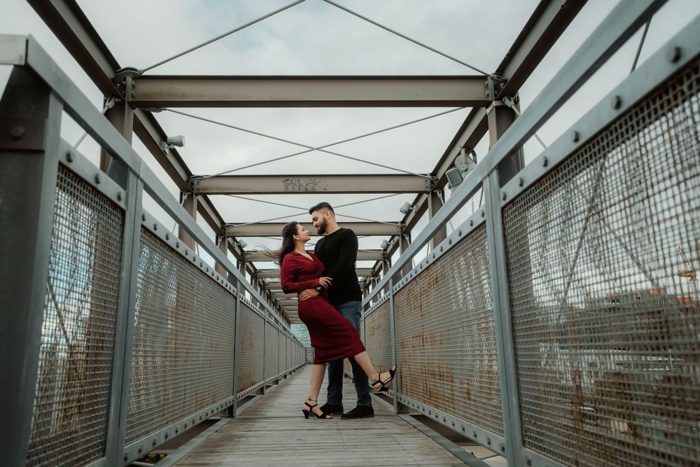 A couple embraces on a covered metal footbridge during a romantic photoshoot.