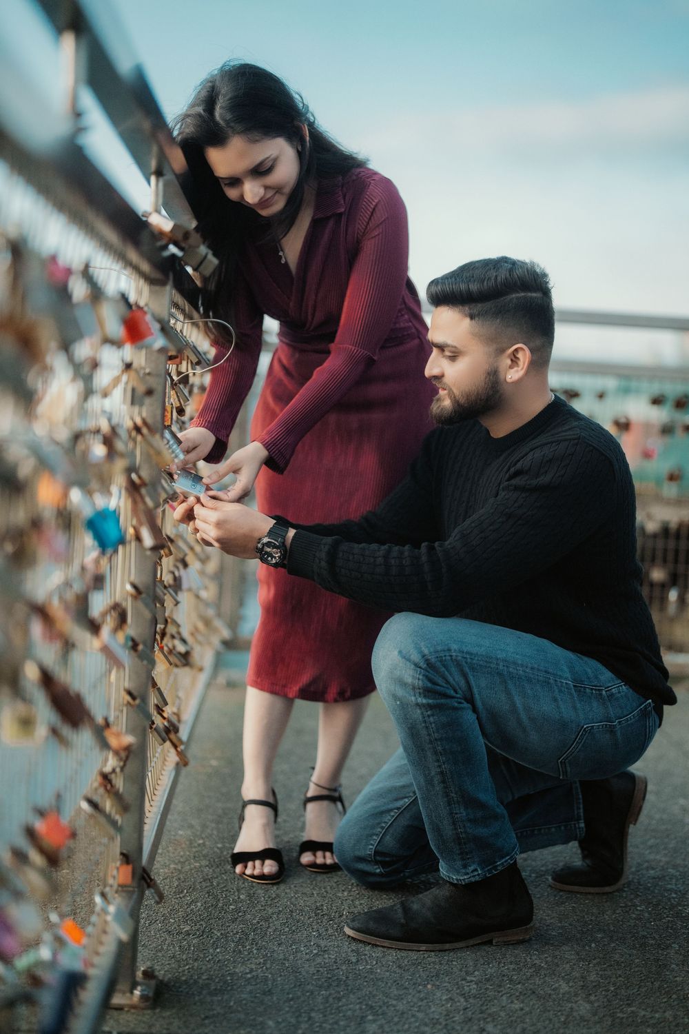 A couple attaching locks to a bridge railing in a romantic tradition under cloudy skies.