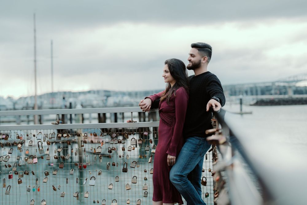 A couple stands at a dock overlooking a scenic marina filled with boats on a cloudy winter day.