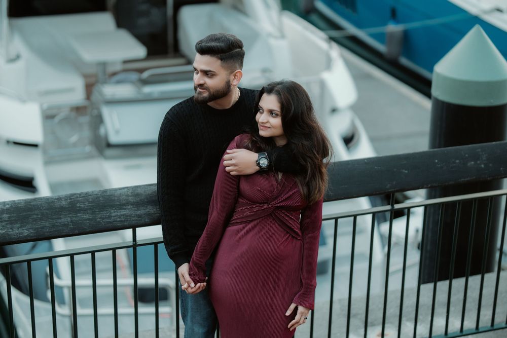 Couple in burgundy outfits embracing during a romantic photoshoot at a harbor boardwalk.