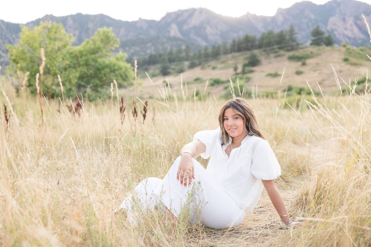 A dreamy scene with someone resting amidst golden wheat fields at sunset with majestic mountains in the background.