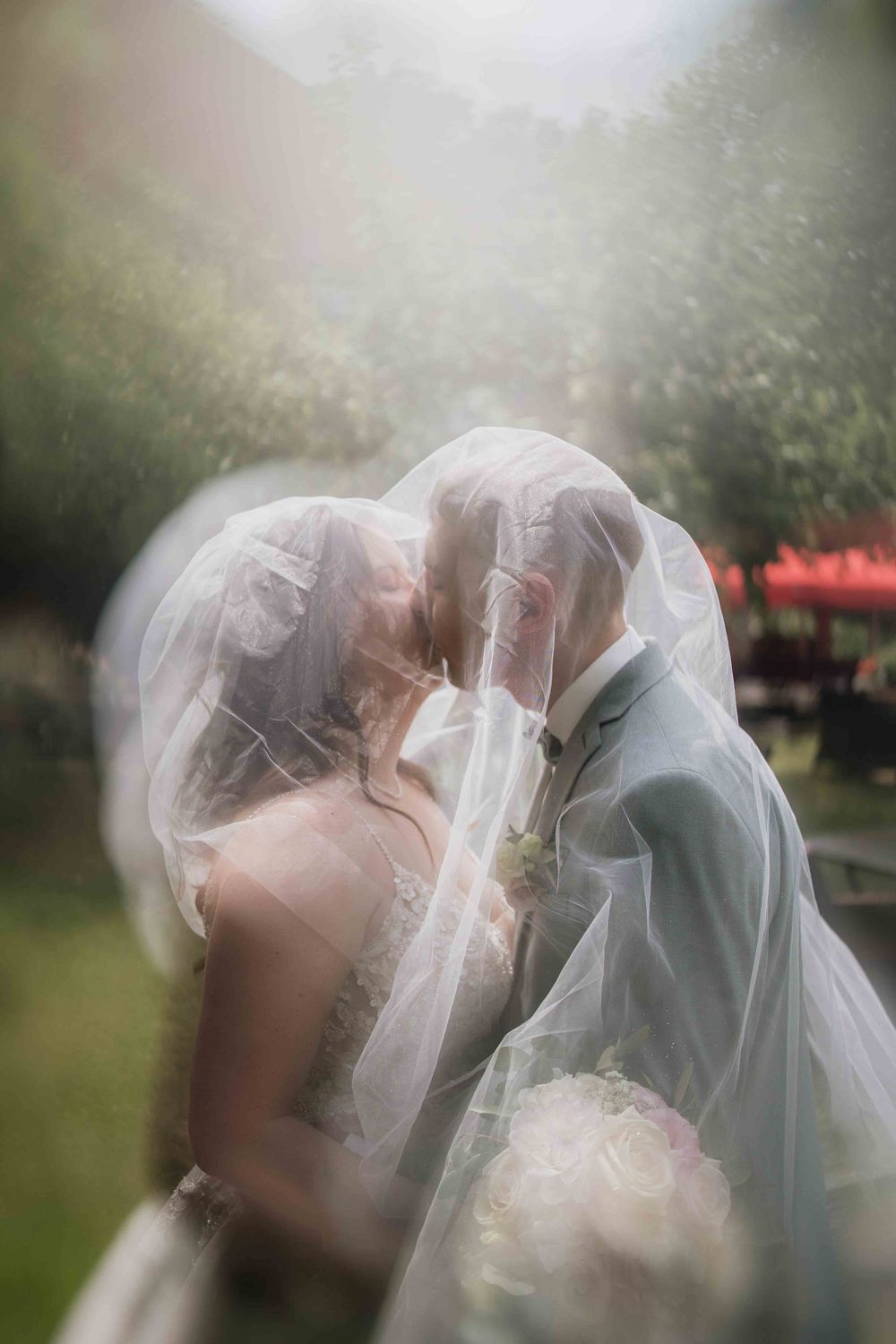 A romantic wedding moment captured through a delicate veil in a garden setting with soft lighting.