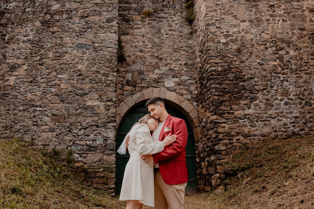 A couple embraces against an ancient stone wall backdrop.