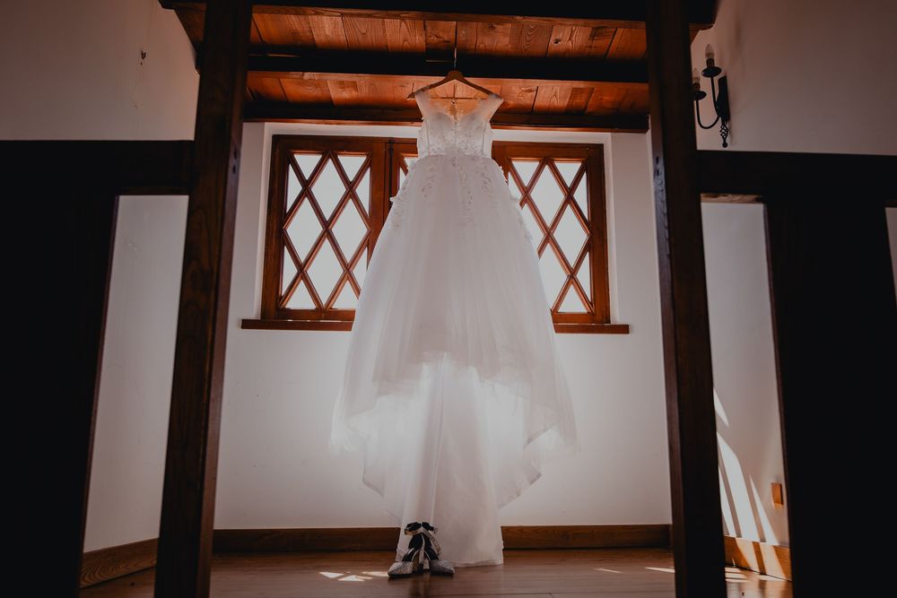 A white wedding dress hangs elegantly against wooden beams and windows.