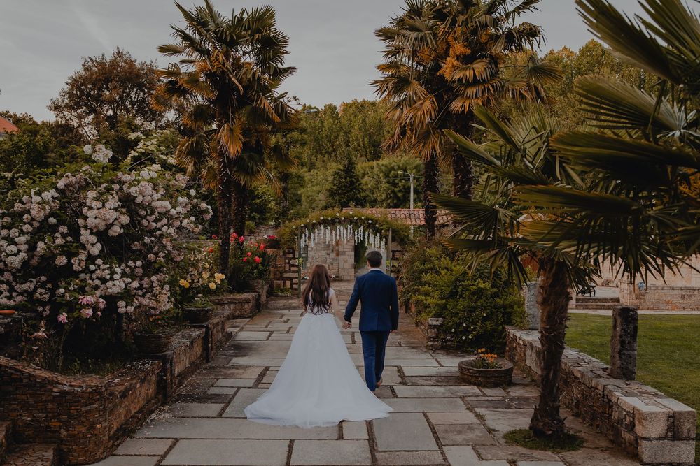 Palm trees line a stone pathway in a romantic garden setting at sunset.