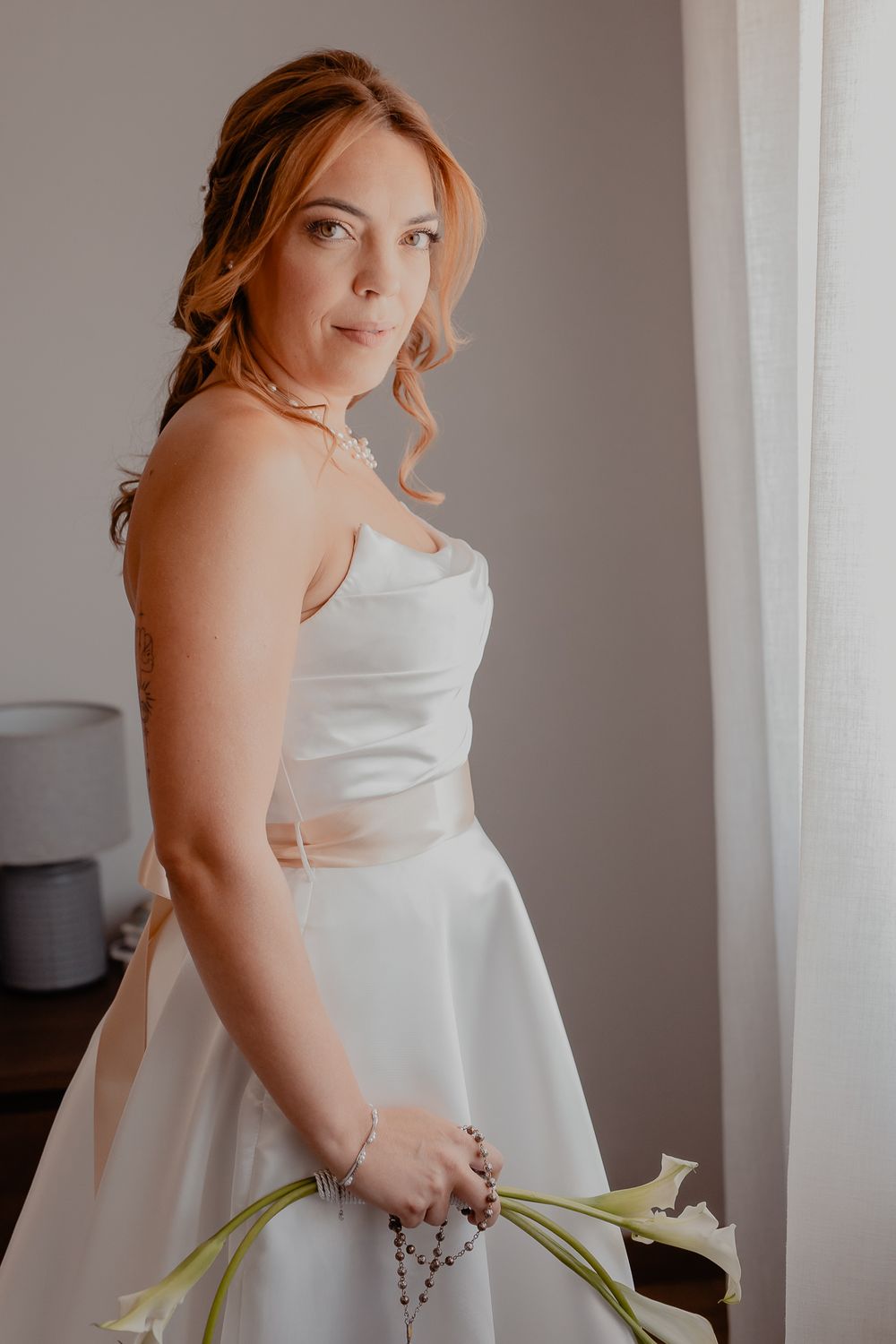 Person in elegant white wedding dress holding bouquet against neutral background.