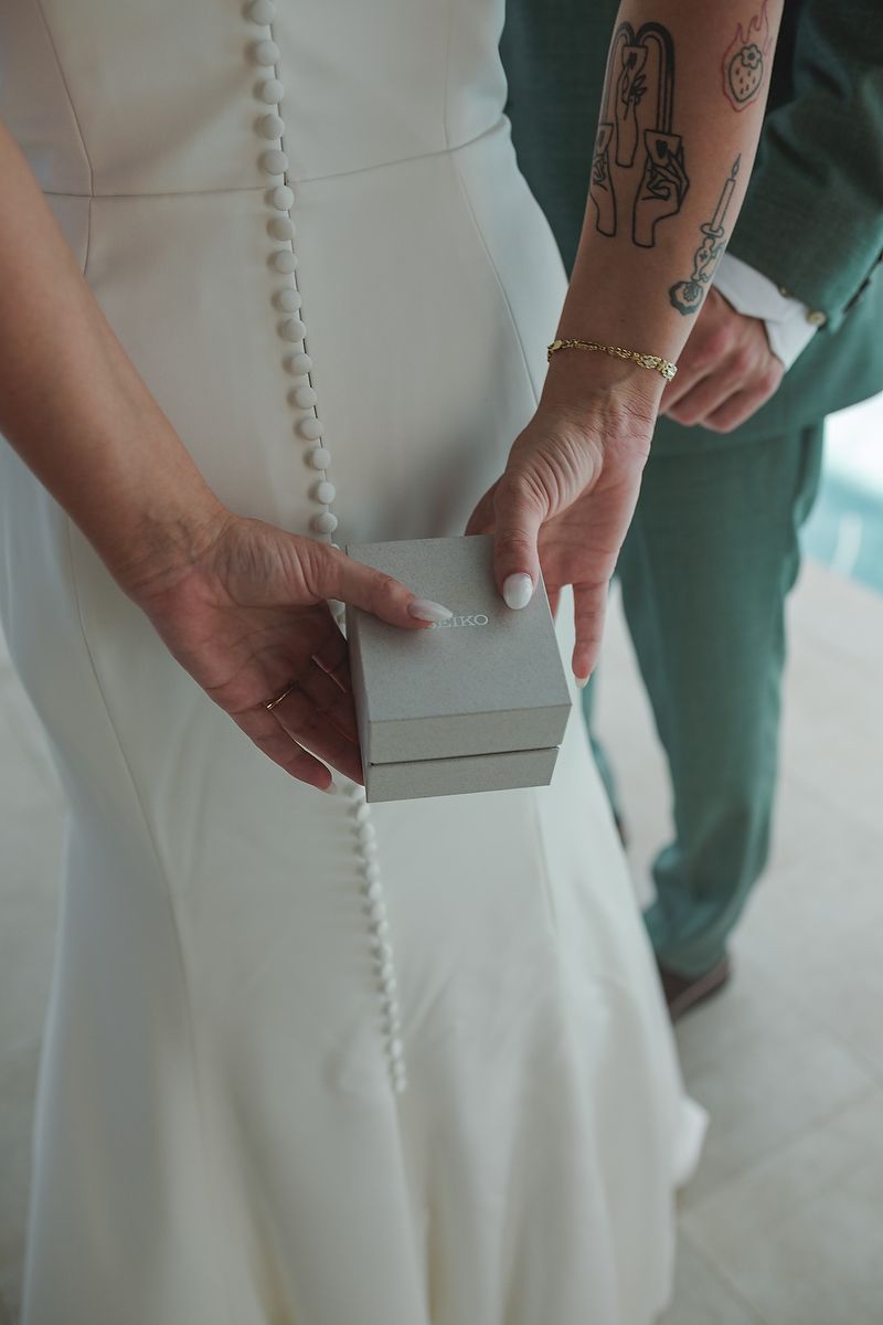 Close-up details of a white wedding dress with button details and visible tattoo on nearby hand.