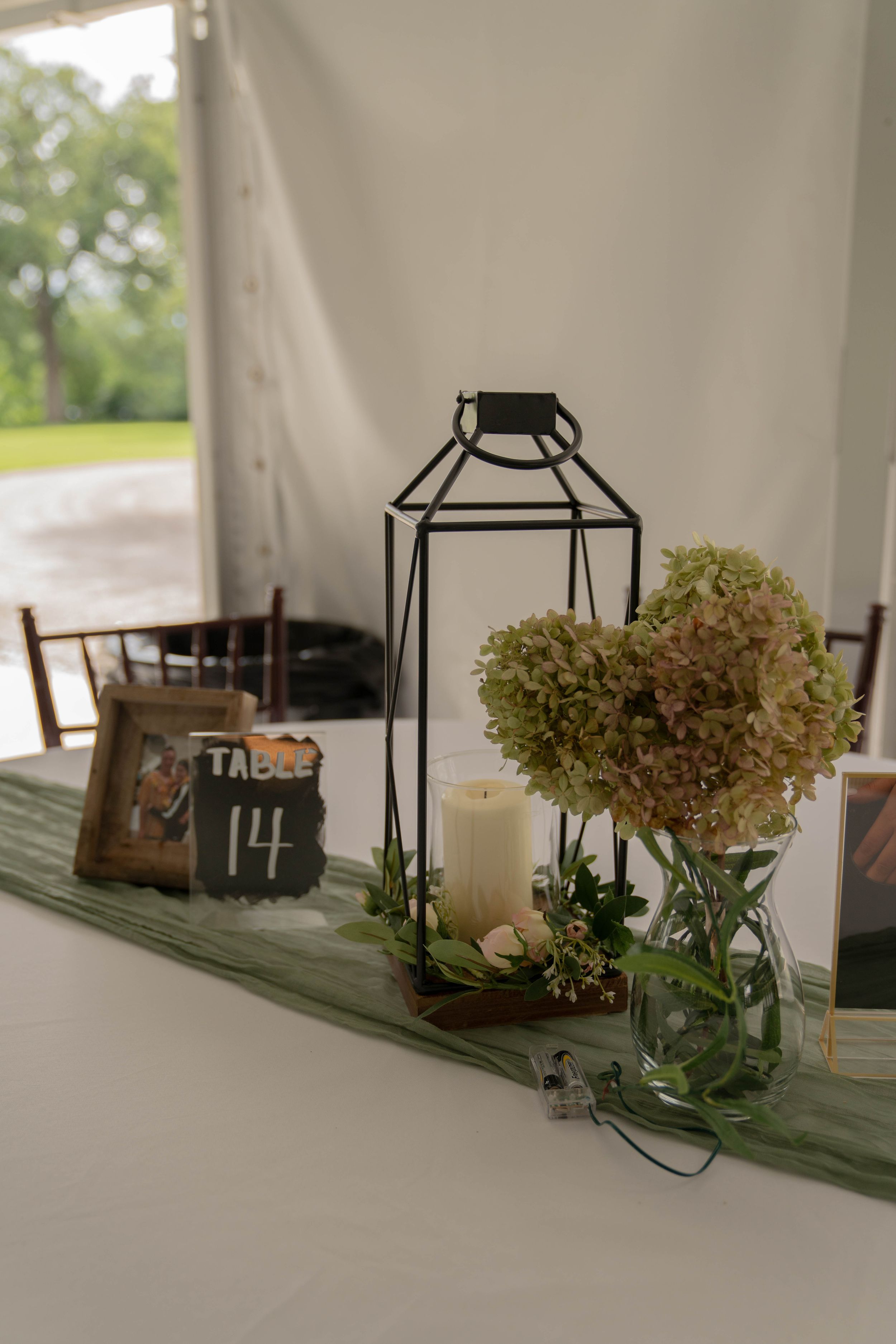 Wedding table centerpiece with dried hydrangeas and rustic lanterns on a green table runner.