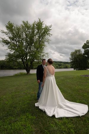 Wedding couple posing by a lake with dramatic cloudy sky and trees in background.