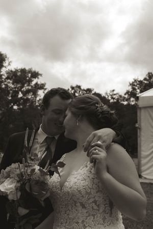A romantic black and white wedding photo of a couple sharing a tender moment with bouquet in hand.