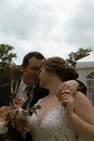 An intimate wedding portrait showing a couple embracing while holding a peach-colored floral bouquet.