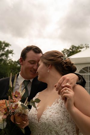Romantic wedding moment captured against cloudy sky with floral decorations.