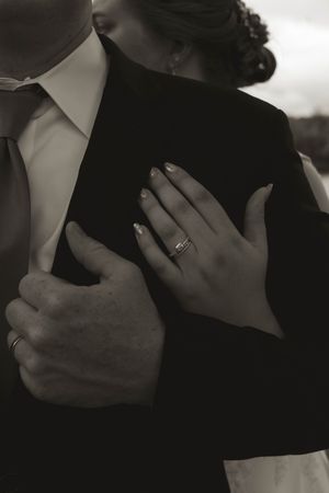 A close-up black and white photo showing hands with wedding rings during an embrace.