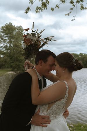 Couple sharing intimate moment by lakeside during wedding celebration.