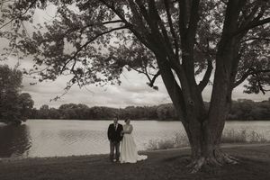 Black and white photo of a couple standing under a large tree by a lake.