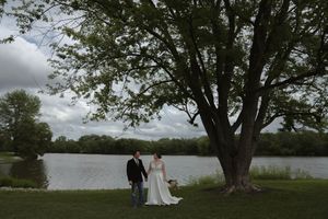 Wedding couple standing by a lake under a large tree on an overcast day.