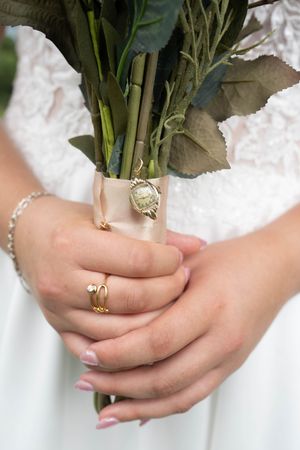 Close-up of hands holding wedding bouquet showing engagement and wedding rings.