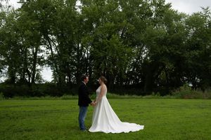 A wedding couple stands together in a lush green field with trees in the background.
