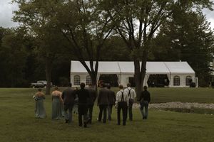 A group of wedding guests walking towards a white tent reception venue on a cloudy day.