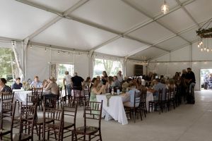 A spacious white wedding tent set up with elegant tables and chairs for a reception.