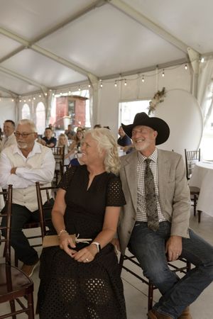 Wedding guests in formal attire seated inside a white reception tent during celebrations.