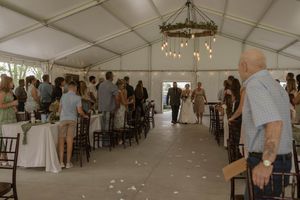 Wedding reception setup in a white tent with elegant lighting and dark wooden chairs.