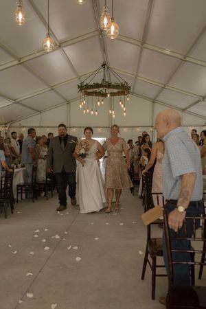 Wedding guests dancing and celebrating inside a white tent with hanging lights.
