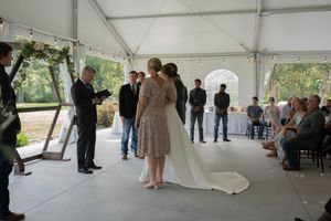An intimate wedding ceremony takes place under a white tent with guests looking on.