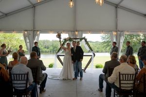 A wedding ceremony in progress inside a white tent with guests seated on both sides of the aisle.