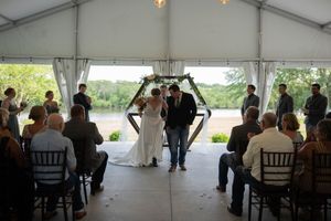A wedding ceremony view from the back of the tent showing guests and the decorated aisle.