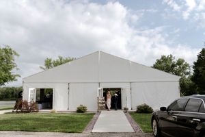 Large white wedding tent set up outdoors with cars parked nearby.