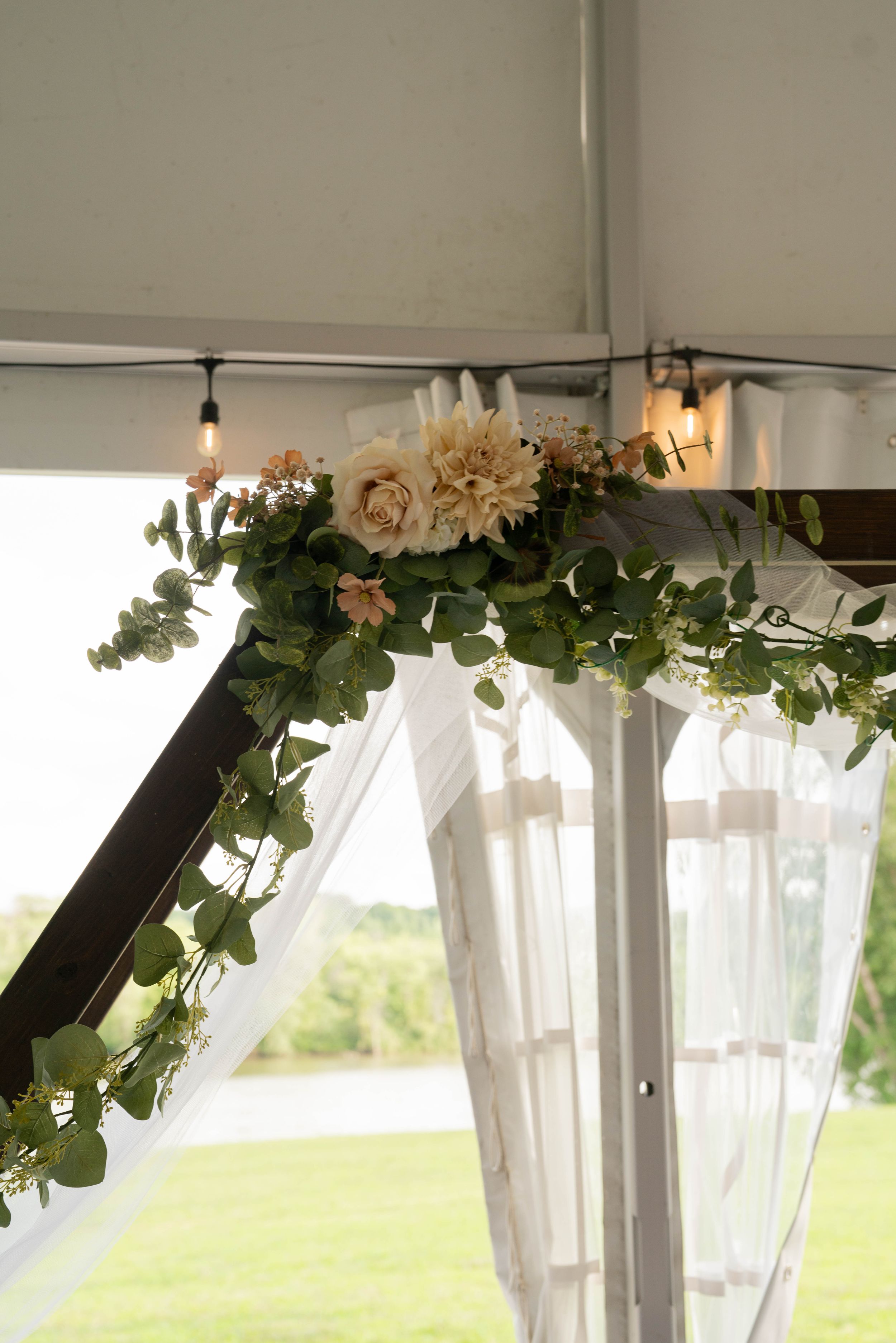 White tent decorated with floral garlands and sheer drapes for outdoor wedding.