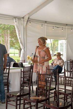 Guest mingling in an elegant white tent reception area with string lights and wooden chairs.