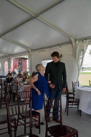 Two people conversing between wooden chairs at an indoor wedding venue.