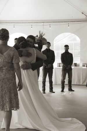 Wedding party members in formal attire gather on a white dance floor under a tent.