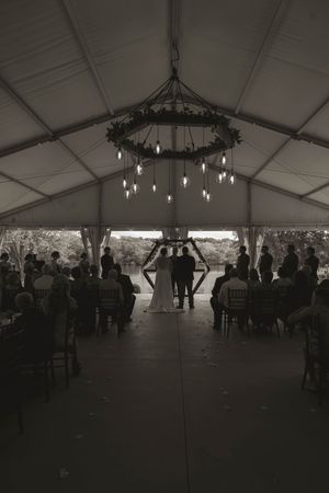 Interior view of a large white wedding tent with chandeliers and guests mingling in the background.