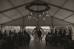 Panoramic view of a spacious wedding reception tent with elegant lighting fixtures and scattered guests.