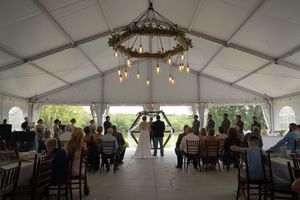 Wide-angle shot of an outdoor wedding tent setup with tables, chairs and decorative lighting.