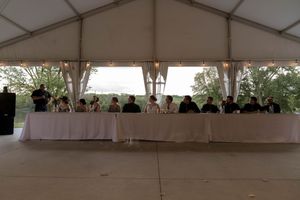 A silhouetted view of wedding guests seated at tables inside a reception tent.