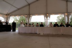 Interior of a white wedding reception tent with tables and guests seated along the perimeter.